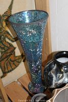Tall iridescent crackled glass vase next to black ceramic marbled vase on a wooden shelf