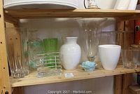 Shelf with various glass and ceramic vases, a small blue ceramic flower, and a Mikasa picture frame