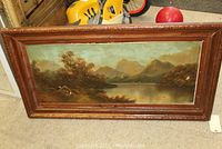 Full view of the framed landscape painting showing the lake, trees, and mountains.