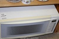 Front view of Panasonic microwave showcasing white door with window and horizontal handle under wooden shelf with dishes above.