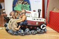 Nautical figurine showing a fisherman holding a net sitting on a boat with wave details