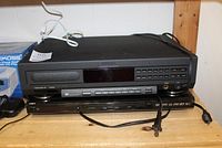 Philips Compact Disc Player CD 920 and Insignia DVD player stacked on wooden shelf with cords visible.