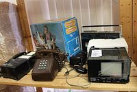 Photo showing all items on a shelf: slide projector in box, 2 retro phones, Chinon camera, Viking radio/cassette player, Crown mini TV radio.