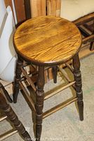 Single wooden bar stool showing round wood grain seat and turned legs with stretchers.