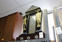 Full view of a black wooden framed mirror with a triangular pediment top and classical male figure prints on the side panels, with decorative circular motifs at the base.