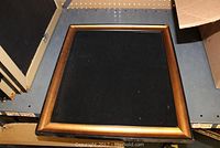 Top view of a jewelry display board with a golden brown wooden frame and black velvet fabric insert.