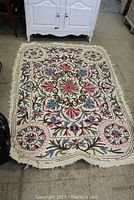 Full view of one of the felt rugs with colorful wool embroidery on cream background, floral and geometric motifs visible, fringed edges.