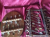 Two spoon racks with souvenir spoons displayed, one wooden and one plastic with ornate carvings.