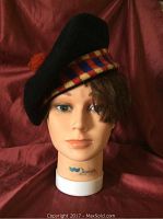 Front view of black Glen Allan curling tam on mannequin head showing red and yellow checkered band and red pompom on top.