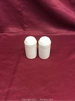 Front view of a pair of white ribbed salt and pepper shakers on a red fabric background.
