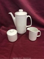 Front view of the coffee set showing coffee pot, creamer, and sugar bowl on burgundy fabric background.