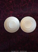 Top view of two white ceramic saucers with ribbed edges on dark red patterned background, used to serve small bowls or gravy boats, approx 7 inches diameter.
