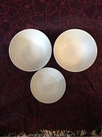 Top view of three white ceramic Johnson Bros Athena pattern serving bowls on a dark patterned surface showing two larger and one smaller bowl.