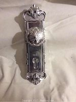 Front view of silver-colored aluminum door knob wall hook with detailed decorative face plate including keyhole design.