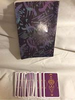 Photo showing purple back side of tarot cards laid out with the tarot book cover in the background, book has dark mystical design.