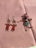 Photo of colorful dancing people earrings and pin on pink cloth background