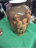 Front and side views of a brown ceramic vase with creamy cherub figures and subtle gold vein decoration on a green cloth background.
