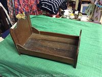 Side view of the vintage oak doll bed showing the flat bed base and the high headboard with scalloped edges.