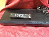 LG Blu-ray DVD player with remote control on top, showing front face and top surface.