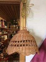 Handwoven wicker swag lamp hanging on a wooden beam, showing the full outer view and scalloped edges