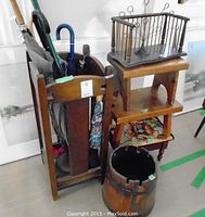 Oak Arts and Crafts style umbrella stand holding multiple umbrellas, small wooden bookshelf on a wooden stool, metal photo tree on top, churn bucket and wooden stools visible around.