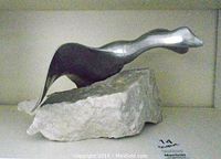 Front and side angled view showing smooth and flowing metal bird form on natural rock base