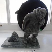 Front view of entire carving: standing Inuit figure in parka with removable walrus on rectangular base