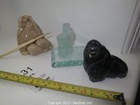 Lot of three sculptures: beige soapstone figure with stick, black stone walrus, and frosted glass Inukshuk paperweight on square base.