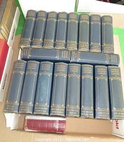 Top down view of the 18 volumes of Charles Dickens Library collection arranged in two rows, blue hardcover with gold embossed title on spine.