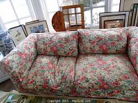 Front view of a floral fabric upholstered sofa with loose cushions and colorful floral pattern.