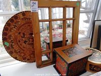 Photo of wooden framed mirror with multiple glass panels and large round carved wood art behind on table.