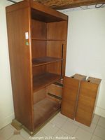 Full view of the faux wood bookcase with two drawers removed and placed on the side, showing three shelves and empty drawer compartments