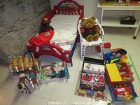 Red Disney Cars toddler bed with mattress, bedding, teddy bear on child's chair, plastic horses, vintage dolls, and various LEGO and toy vehicles arranged on floor.