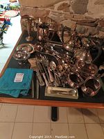 Wide shot of entire assortment on black surface showing hollowware, utensils, trays and vase