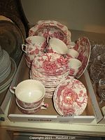 Overall box view of the Johnson Bros dish set including stacked saucers, cups, side plates, and bowls in red English Chippendale pattern.