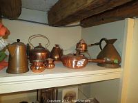 Shelf display showing seven copper pieces: two kettles, a pan with lid, a large pitcher, tall pot, and two small pots