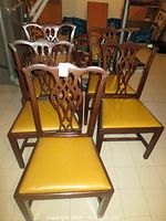 Front view of four standard dining chairs with press back design and yellow vinyl seats