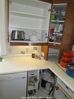 Kitchen cabinet with stainless steel toaster, white electric kettle on shelf, countertop with orange cookware and various kitchen items.