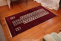 Full view of rectangular hand woven Persian carpet on wooden floor, showing the main red field with central white rectangular design with burgundy leaf/tree shapes and smaller white rectangular motifs.
