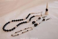 Full view of the jewelry lot with a black onyx and sterling silver beaded necklace, bracelet, four pairs of earrings of various designs, and a ring on a display cone.