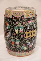 Frontal image showing black porcelain garden stool with colorful floral and butterfly designs, and red bead accents.