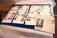 Layout of more than 85 First Day Covers displayed on blue cloth showing various stamps and postmarks