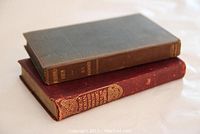 Two vintage books lying flat, showing spines and covers, red leather bound Koran and gray cloth bound Mohammedanism.