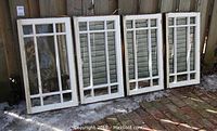 Four white-painted wood sash windows leaning against fence outdoors