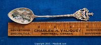 Full length view of the silver souvenir spoon alongside a ruler showing 5 1/4 inch length, with intricate handle design and enamel decoration.