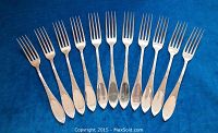 Twelve forks laid side by side on blue cloth