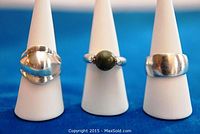 Three vintage modernist sterling silver rings displayed side by side on white ring holders against a blue background.