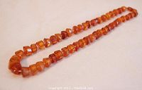 Full view of a carved Baltic amber bead necklace laid flat showing shape and color of beads.