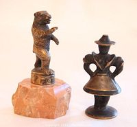 Two miniature bronze sculptures: a standing bear on stone base and a woman figurine in traditional attire, shown side by side.