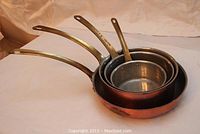 Four nested copper saucepans with brass handles